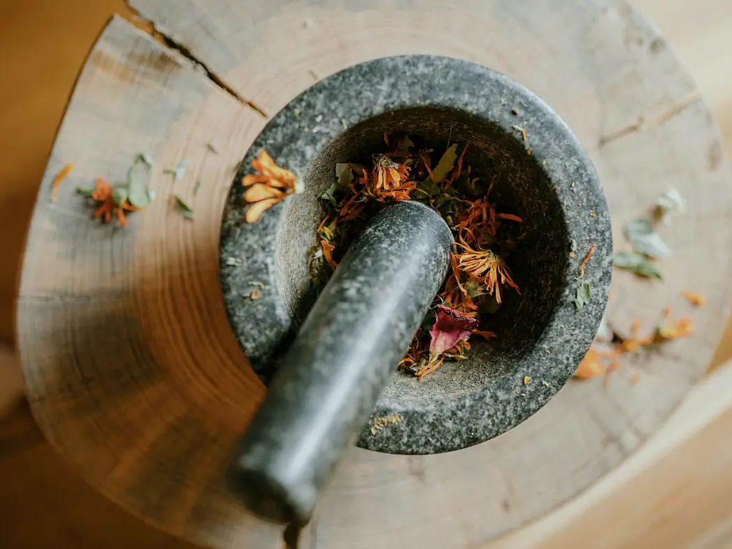 Dried flowers and herbs in a stone mortar with its pestle, on a wooden block.